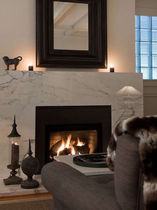 a chic modern nook with a white marble fireplace, some decor on the mantel, a coffee table and a grey chair