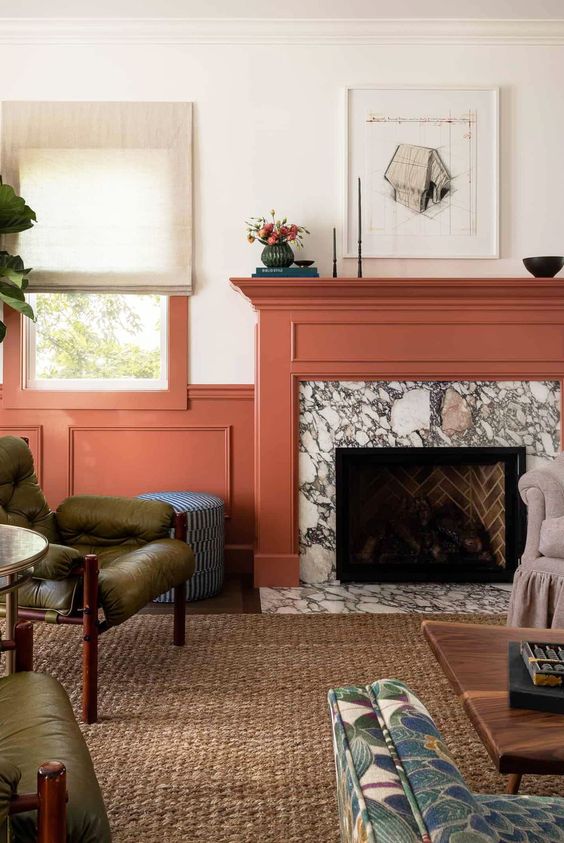 a colorful living room with coral paneling, a marble fireplace with a coral mantel, green chairs, a coffee table and some decor
