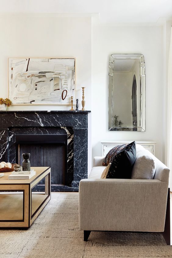 a contrasting living room with a black marble fireplace, neutral seating furniture, a coffee table, a mirror and some decor