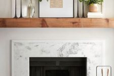 a fireplace with a marble surround, a wooden slab mantel, candles, greenery and an artwork is a stylish idea