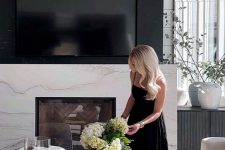 a fireplace with a white marble surround and a black marble piece on top, coffee tables and a large chandelier