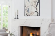 a jaw-dropping fireplace nook with a white marble fireplace, striped chairs, a wooden coffee table and a bold artwork