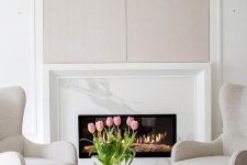 a light-filled neutral and pastel living room with a marble clad fireplace and a cool sitting zone by its side