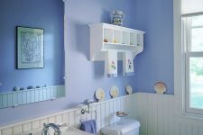 a lovely periwinkle bathroom with white wainscoting, white vintage appliances and a white display shelf plus some seashell decor