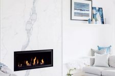 a modern coastal living room with a white marble fireplace, neutral furniture and blue accents for a beachy feel