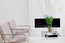 a neutral elegant space with a white marble clad fireplace, lavender chairs and touches of brass for more chic