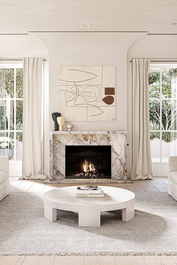 a neutral living room with a marble fireplace, a round coffee table, neutral seating furniture, a large artwork and some decor