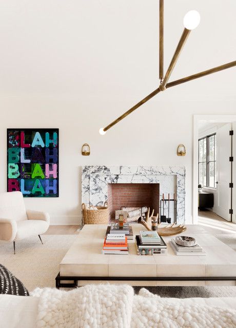 a neutral living room with a marble fireplace, an oversized coffee table, neutral chairs, a tube chandelier and a bold artwork