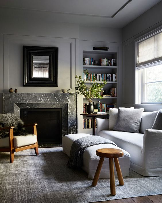 A neutral living room with dove grey walls and built in shelves, a white sofa and a bench, a fireplace clad with black marble