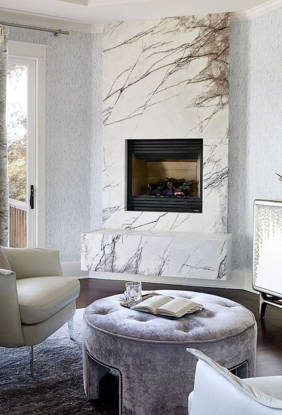 a neutral luxurious living room with a marble clad built in fireplace and refined leather and velvet furniture