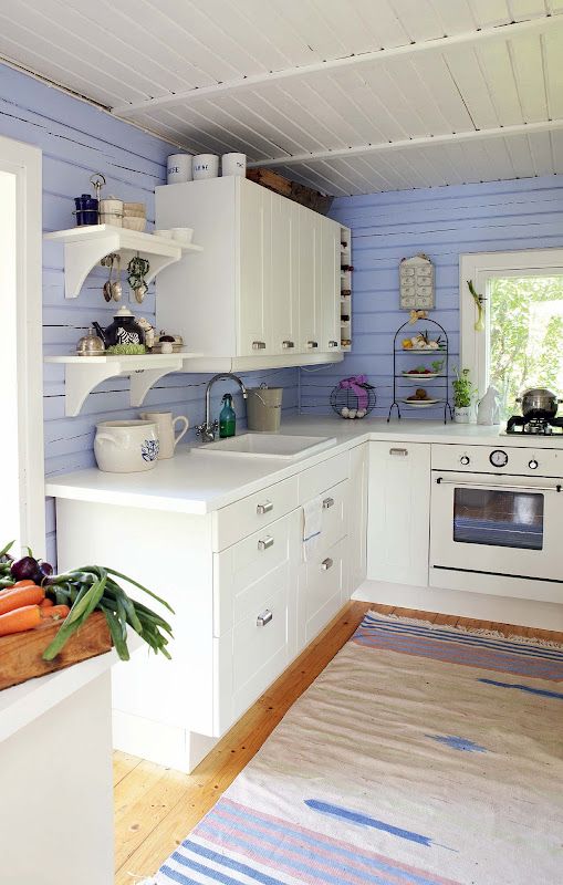 a pretty and chic kitchen with very peri planked walls, creamy cabinets, a dip-dyed rug looks very cute and cottage-like