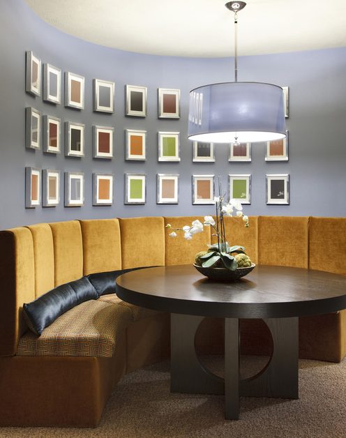 a refined and bold dining space with a round dark stained table, a large curved banquette seating, a colorful gallery wall with color samples