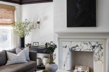 a refined contemporary living room with a white marble fireplace, coffee tables, a taupe sofa, some pillows, a black console