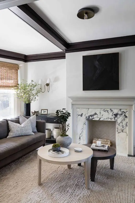 a refined contemporary living room with a white marble fireplace, coffee tables, a taupe sofa, some pillows, a black console