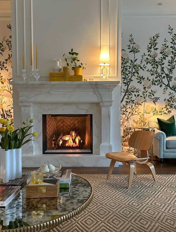 a refined interior with a white marble fireplace, an MDF chair, a table with a golden edge, a printed rug, some greenery and lamps