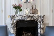 a refined living room with a black cast iron fireplace and a white marble mantel, blue and grey chairs, a mirror over it