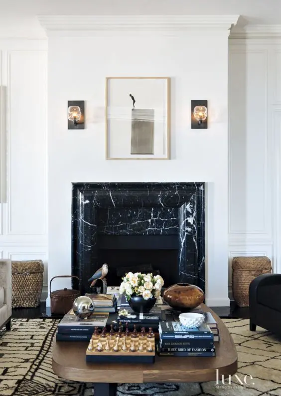 a refined living room with a black marble fireplace, a coffee table with decor, a printed rug and some art