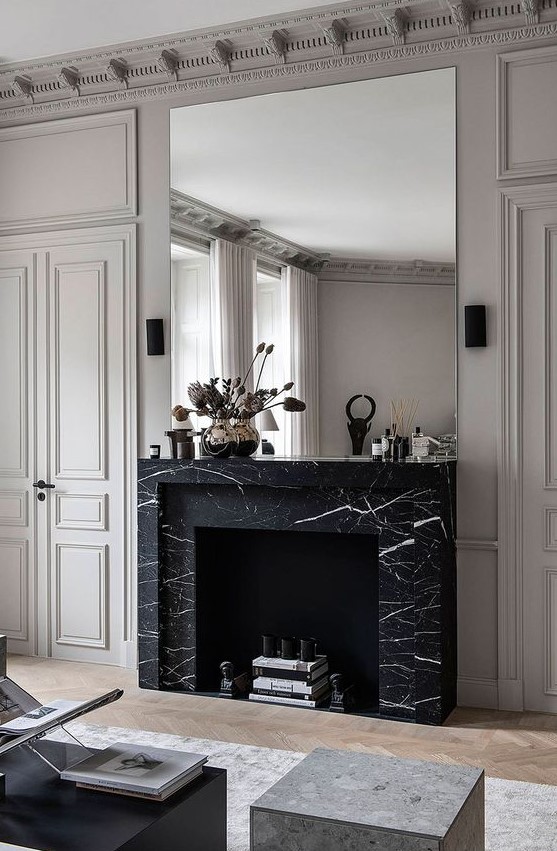 a refined monochromatic living room with a non working fireplace clad with black marble and an oversized mirror over it