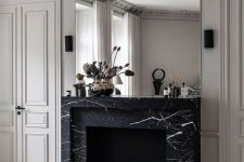 a refined monochromatic living room with a non-working fireplace clad with black marble and an oversized mirror over it