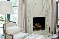 a refined neutral living room with a marble fireplace, a white refined chair and a floor lamp and some decor