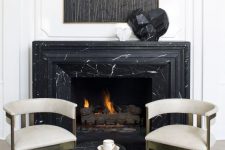 a refined nook with a black marble fireplace and a matching side table, gorgeous brass and velvet chairs