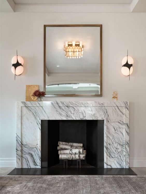 a refined space with a white marble fireplace, a mirror in a gilded frame, sconces, some art and decor is a super chic idea