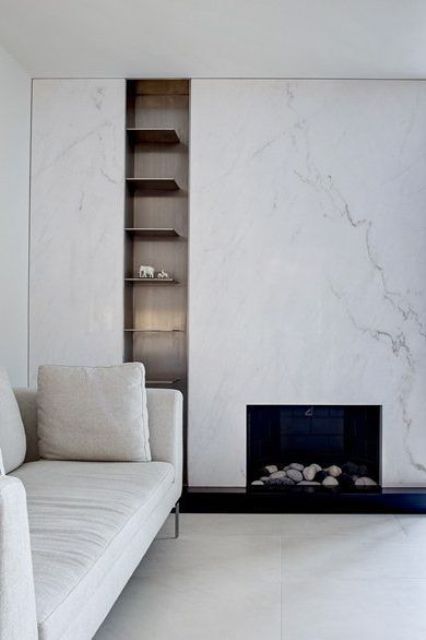 A sophisticated neutral living room in contemporary style, with a white marble fireplace, built in shelves and a white sofa
