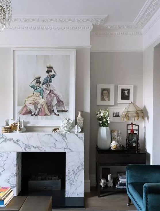a whimsical vintage inspired living room with a non working fireplace clad with white marble and beautiful artworks