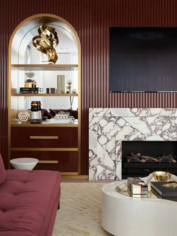 an exquisite burgundy living room with fluted walls and a built-in niche, a white marble fireplace, a burgundy sofa and a round coffee table