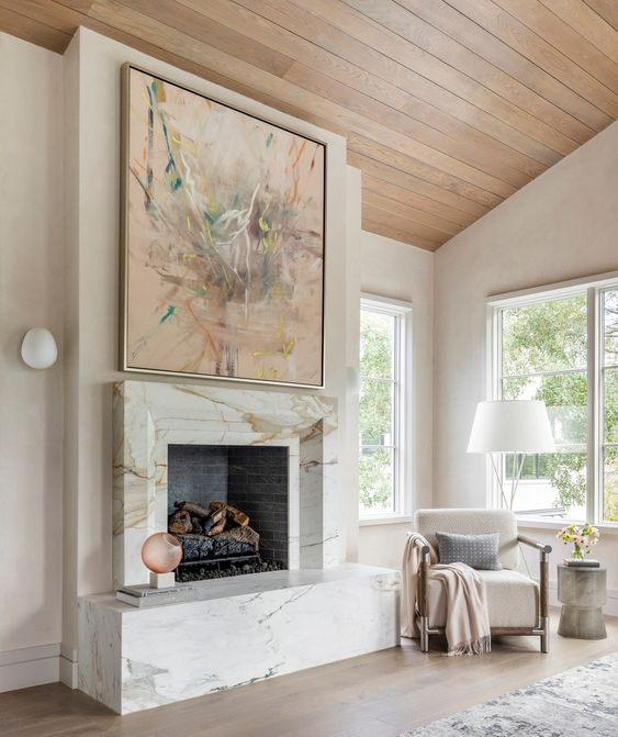 an exquisite fireplace clad with white marble, with an oversized artwork, a white chair, a floor lamp and some textiles