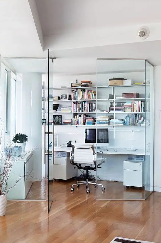 a contemporary glass enclosed home office with open shelves, a desk with storage, a white chair, a sleek white storage unit