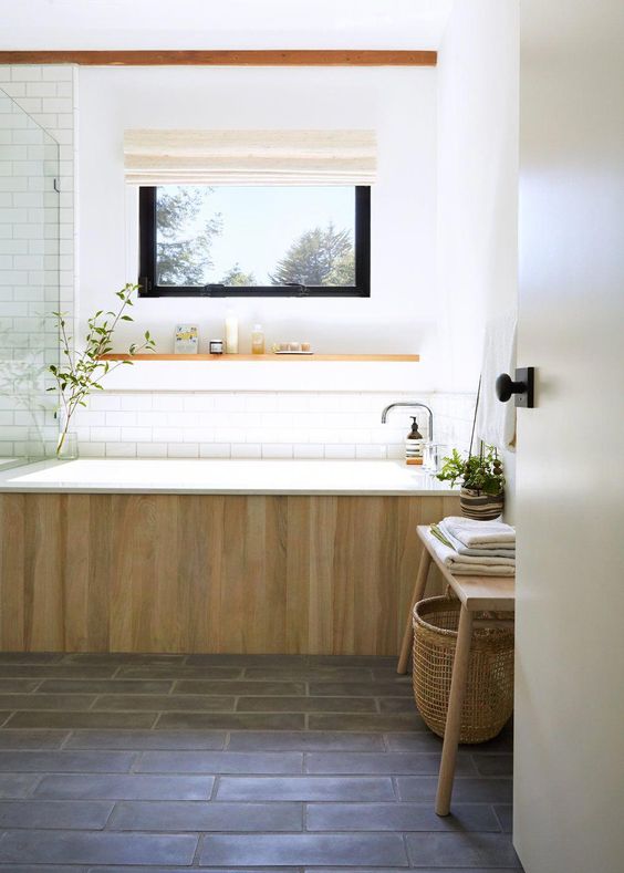 A spa like bathroom in neutrals, with a glass enclosed shower, a bathtub clad with wood and a wooden bench with a basket