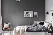 a Scandinavian bedroom with a slate grey accent wall, a white bed with lots of pillows, black sconces and a nightstand