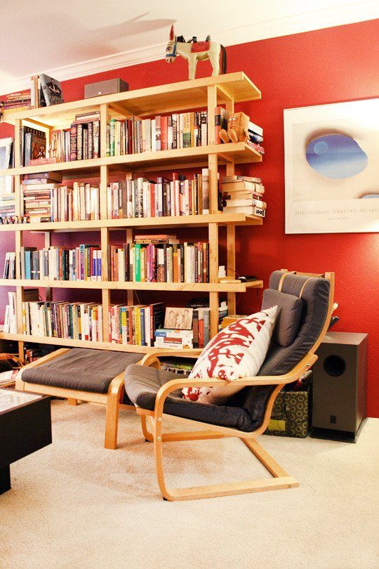 a bold living room with a coquelicot accent wall, a large open bookcase, a grey chair with a footrest, artwork is amazing
