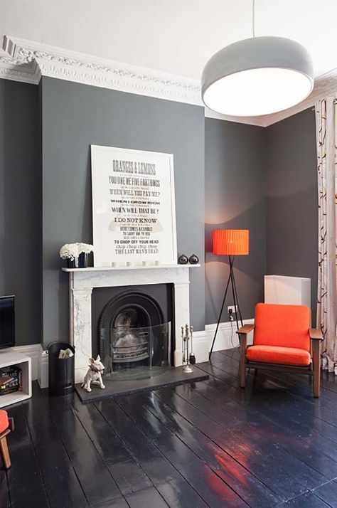 A catchy modern living room with slate grey walls, a fireplace, bold orange pieces   lamps, chairs is a chic and contrasting space