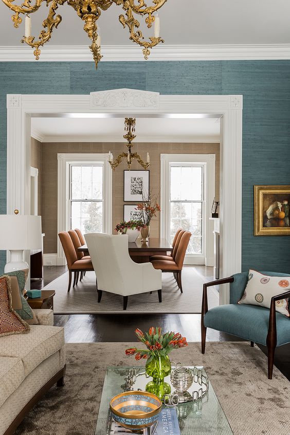 a chic living room with blue grasscloth wallpaper, a neutral sofa and a blue chair plus a refined gold chandelier