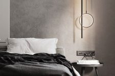 a contemporary bedroom with a grey limewashed wall, a grey iupholstered bed with black bedding, a simple round nightstand