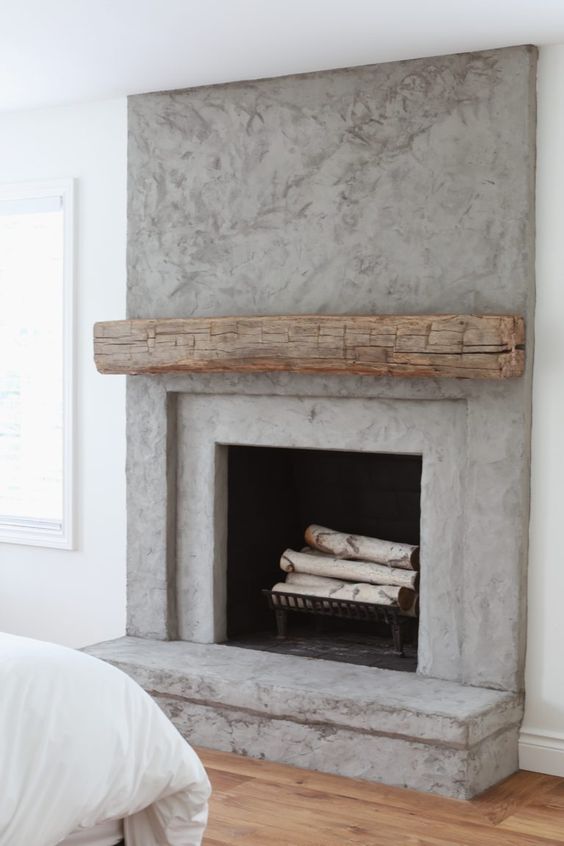 a contemporary concrete fireplace with a rough wood mantel and firewood in the fireplace - the mantel cozies the fireplace up