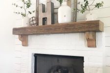 a farmhouse white brick mantel with a rough wood slab mantel, greenery in vases, wooden frames and a wooden basket for firewood