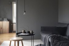 a minimalist living room with slate grey walls, a graphite grey sofa with black blankets, a stained and black table