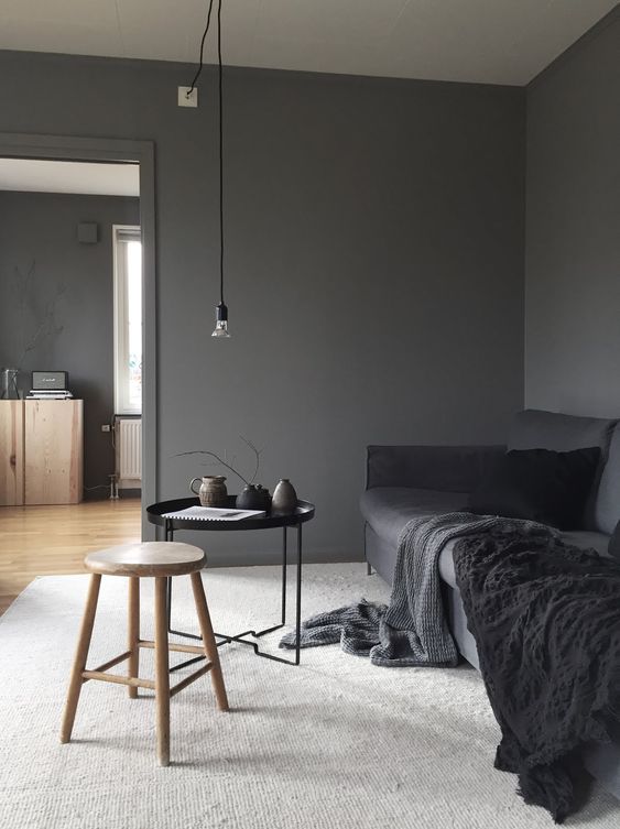 a minimalist living room with slate grey walls, a graphite grey sofa with black blankets, a stained and black table