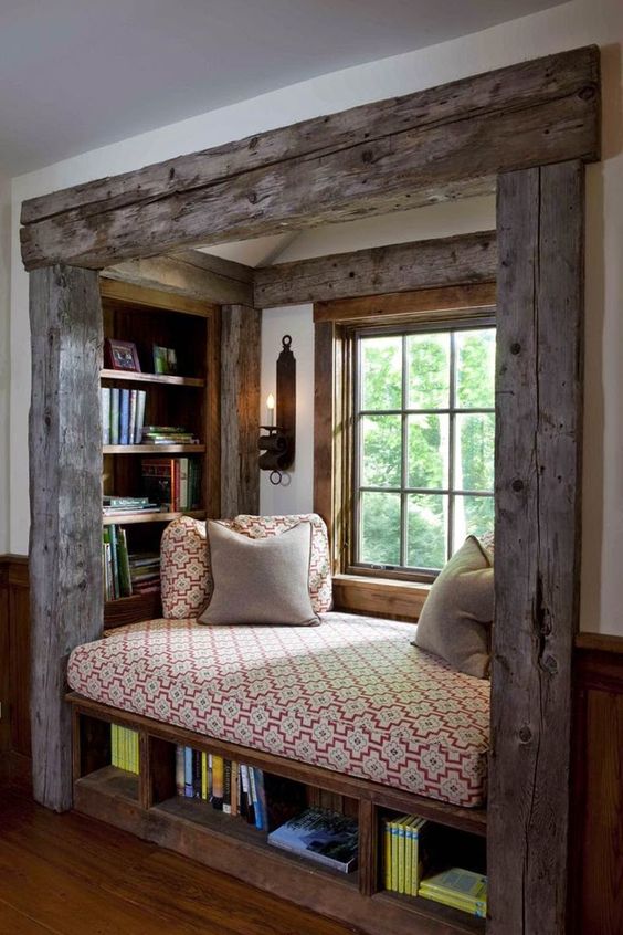 A pretty reading nook with rough and aged wood beams, built in shelves, a daybed with chairs and additional book storage underneath