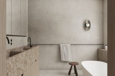 a relaxed bathroom with grey limewashed walls and a floor, a wodoen vanity with stone sinks, an oval tub