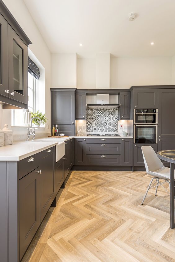 A stylish slate grey kitchen with shaker style cabinets, white countertops, a printed tile backsplash and built in lights
