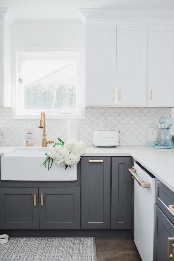 a two-tone kitchen with upper white cabinets and lower slate grey ones, with white stone countertops and white fishscale tiles