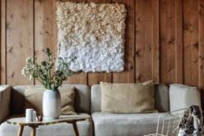 a welcoming neutral living room with rough wood panels, a neutral sofa and pillows, a living edge table and a wire chair plus an ombre wall art
