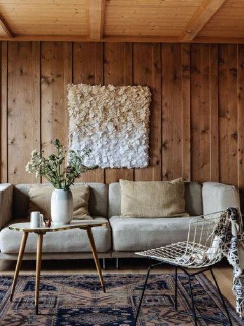 a welcoming neutral living room with rough wood panels, a neutral sofa and pillows, a living edge table and a wire chair plus an ombre wall art