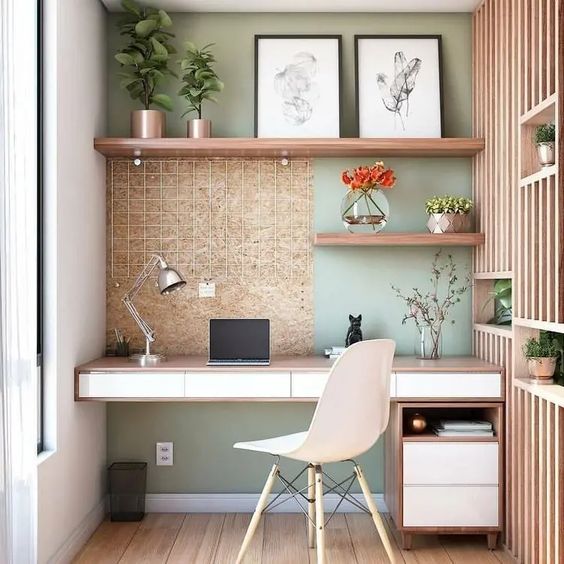 a cozy home office nook with a built-in desk, a white chair, open shelves, a green accent wall and box shelves with various plants