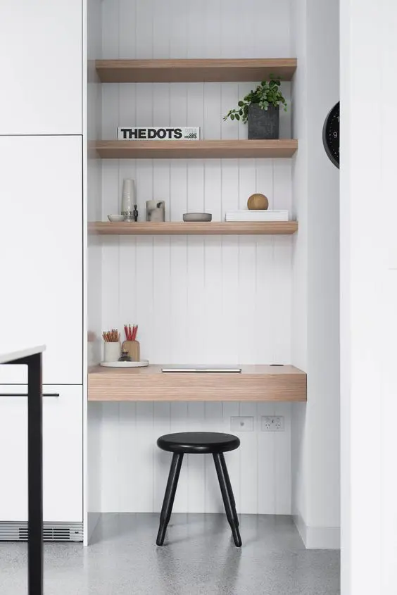 a small home office nook with built-in shelves, a built-in desk, a black stool and a potted plant and books