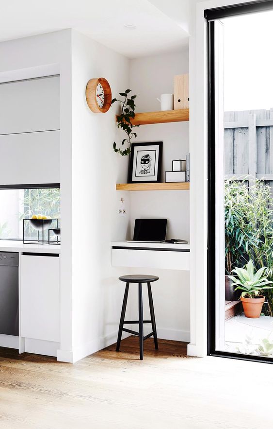 A super tiny working nook with built in shelves and a small desk with drawers, a black stool, artworks and a potted plant
